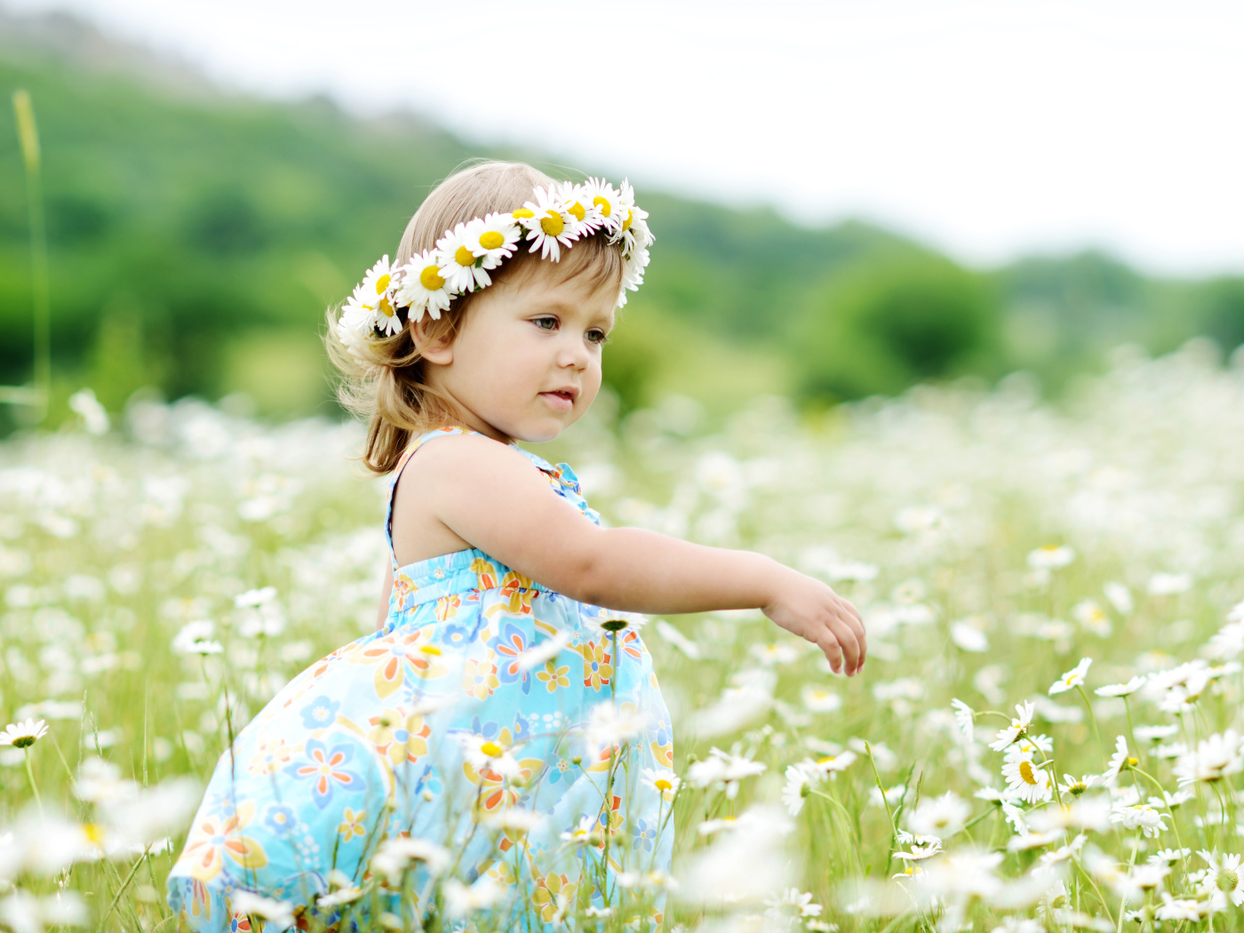 Маленькая девочка с венком на голове гуляет по полю с ромашками