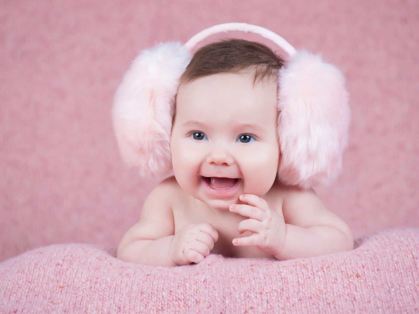 Милый улыбающийся младенец в больших розовых наушниках