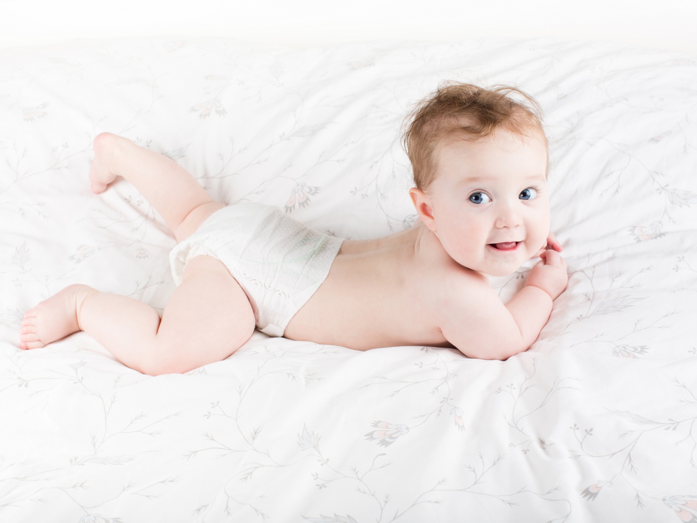Забавный голубоглазый малыш лежит на белом покрывале