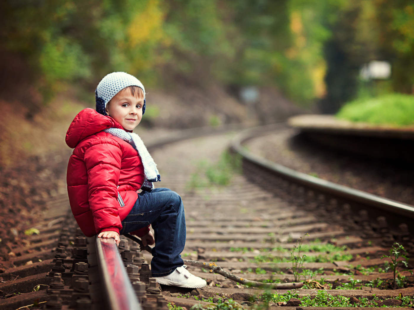 Маленький мальчик в красной куртке сидит на рельсах