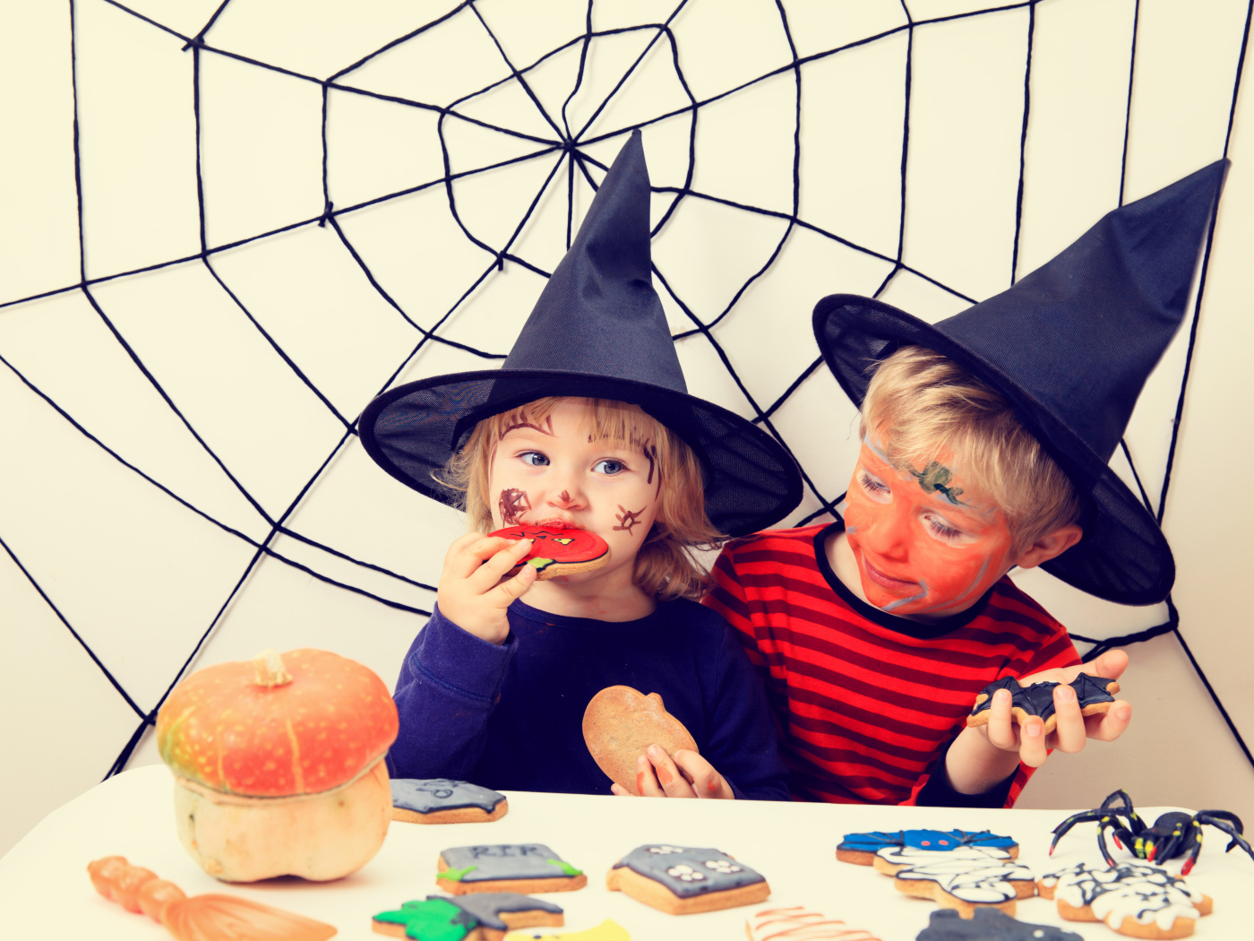 Маленькие дети в костюмах на Хэллоуин едят праздничные сладости