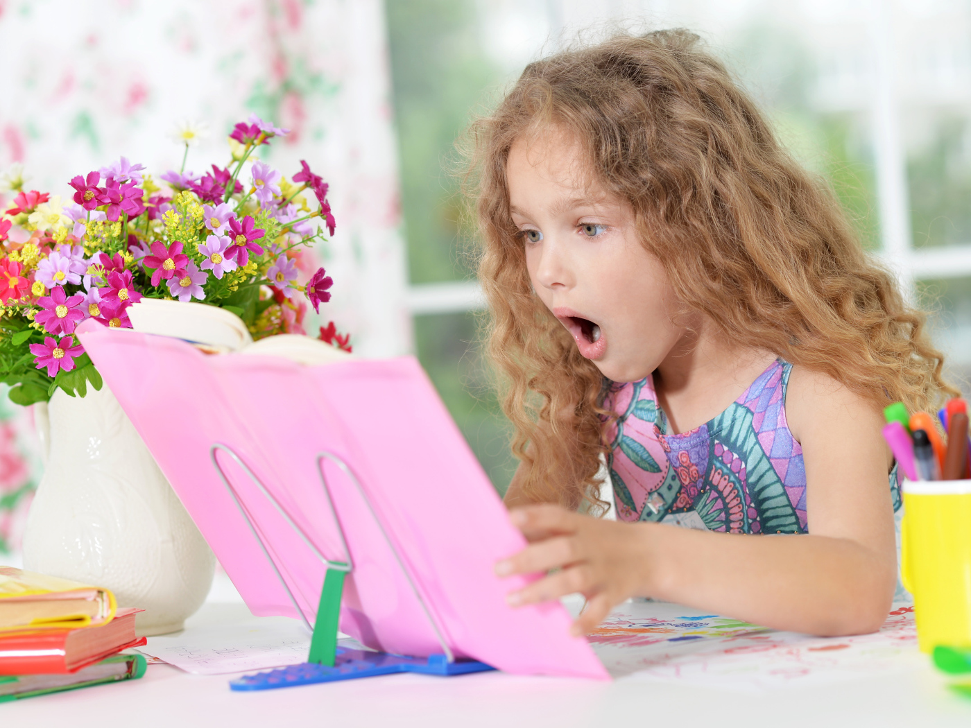 Маленькая русоволосая девочка удивленно смотрит в книгу