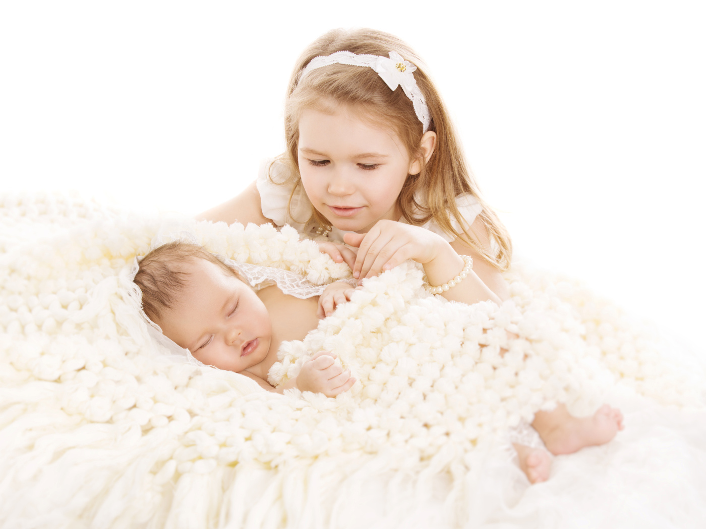 Маленькая девочка в белом со спящим младенцем на белом фоне