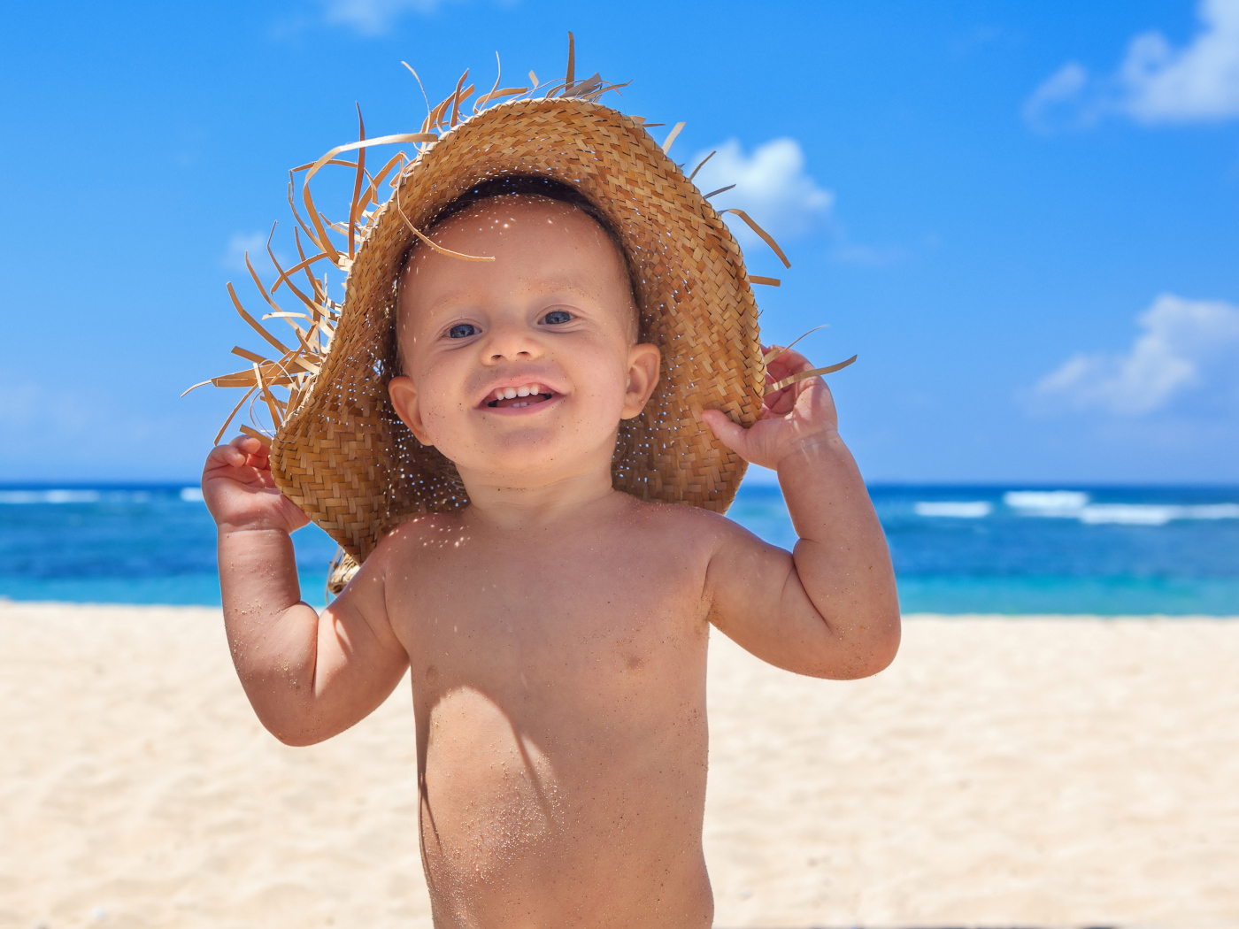 Маленький улыбающийся мальчик в соломенной шляпе на пляже