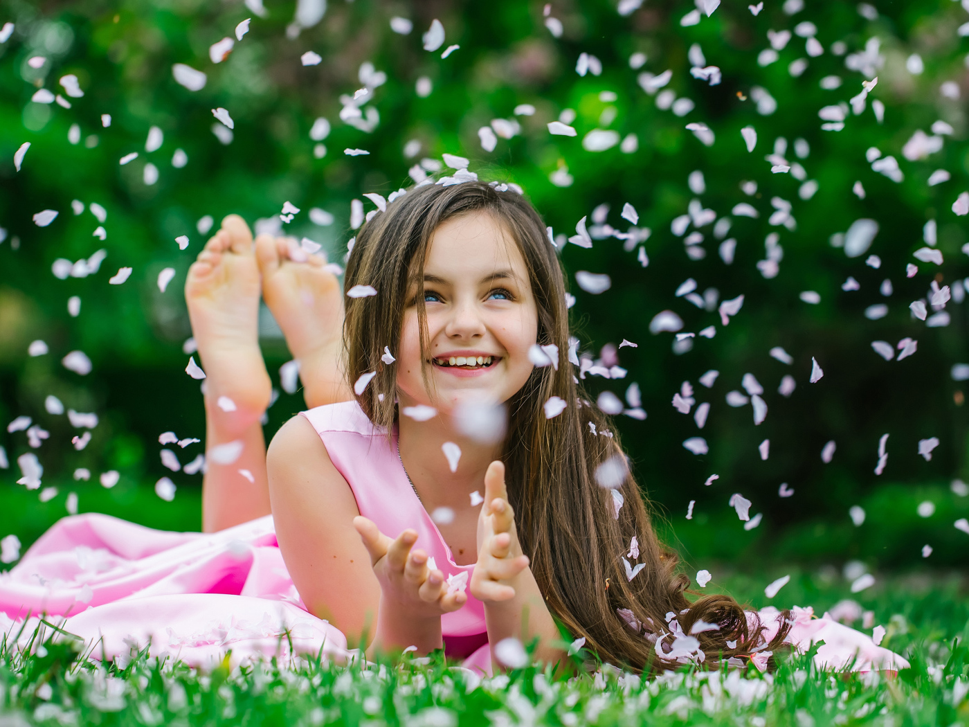 Маленькая улыбающаяся девочка шатенка ловит лепестки