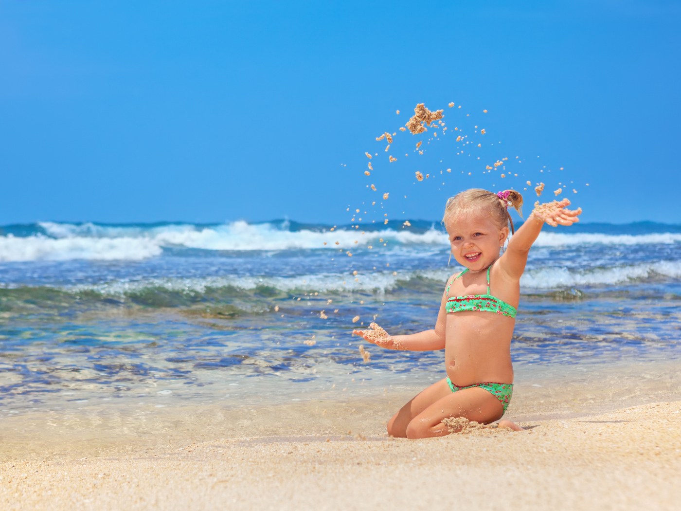 Маленькая улыбающаяся девочка играет на пляже с песком