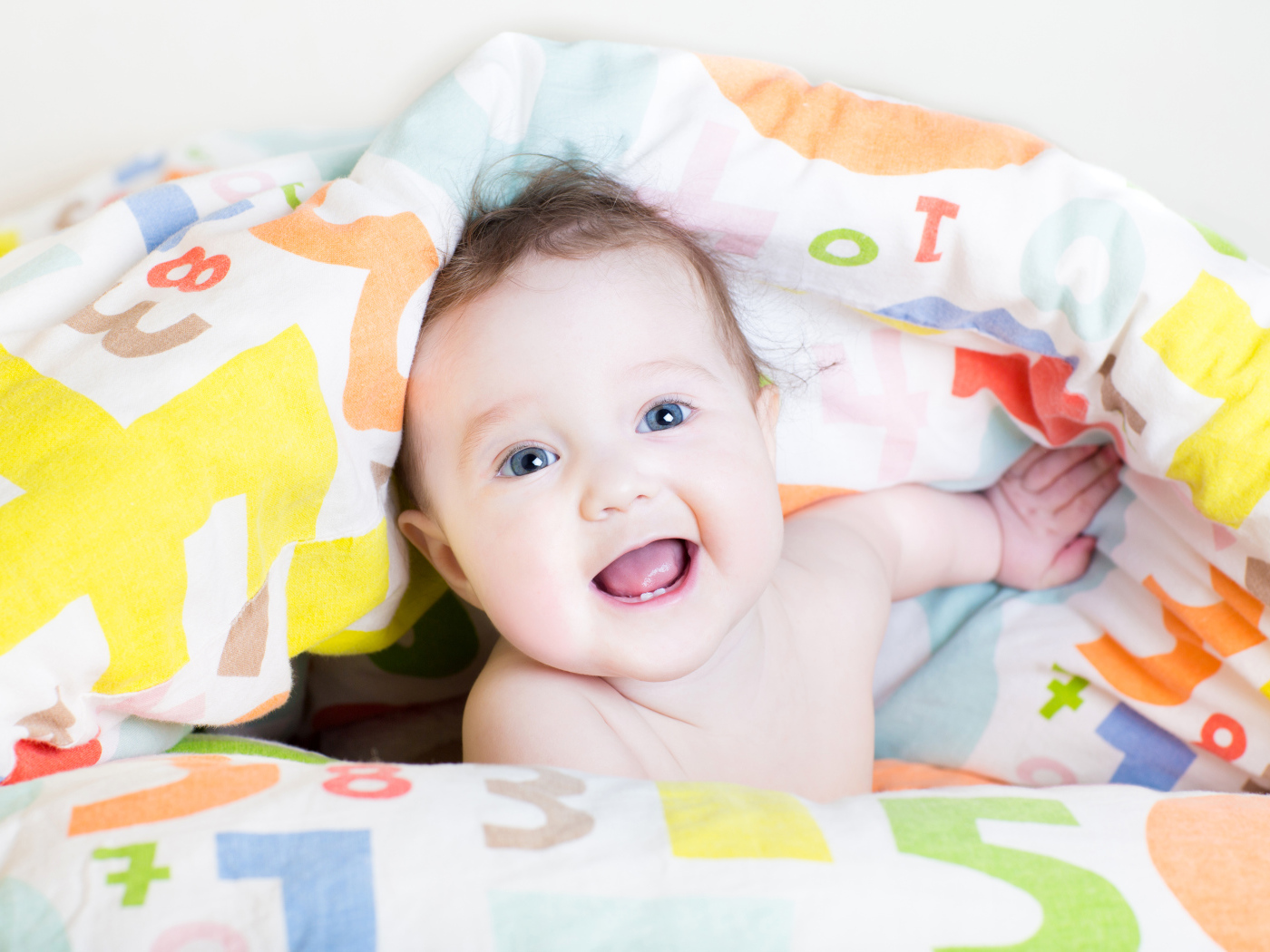 Улыбающийся голубоглазый ребенок под разноцветным покрывалом