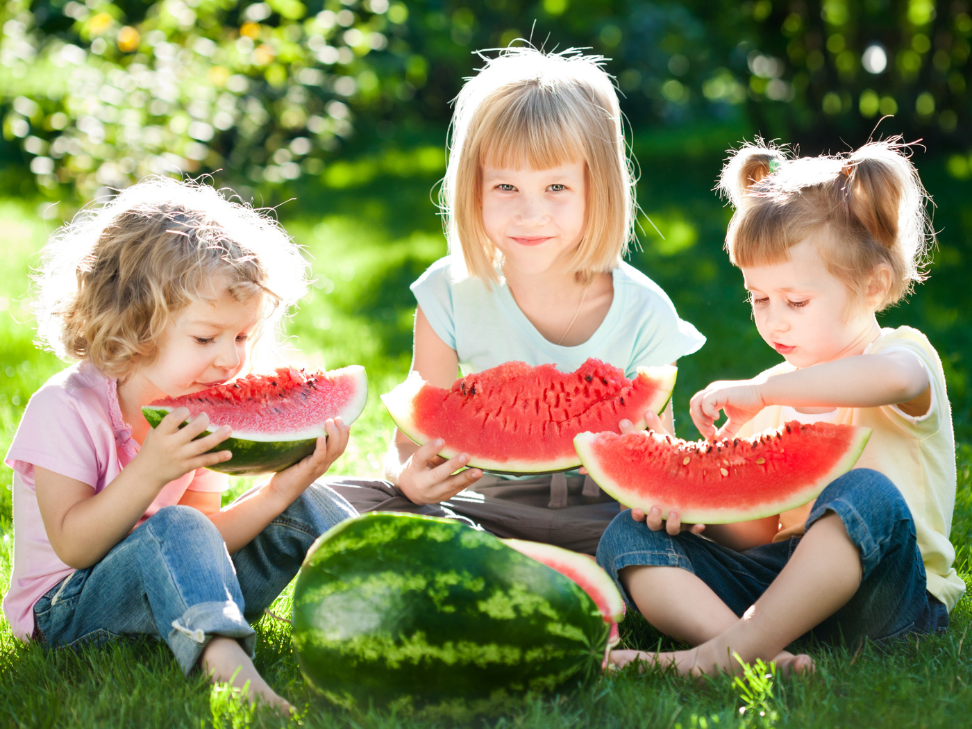 Три маленькие девочки едят арбуз на зеленой траве летом