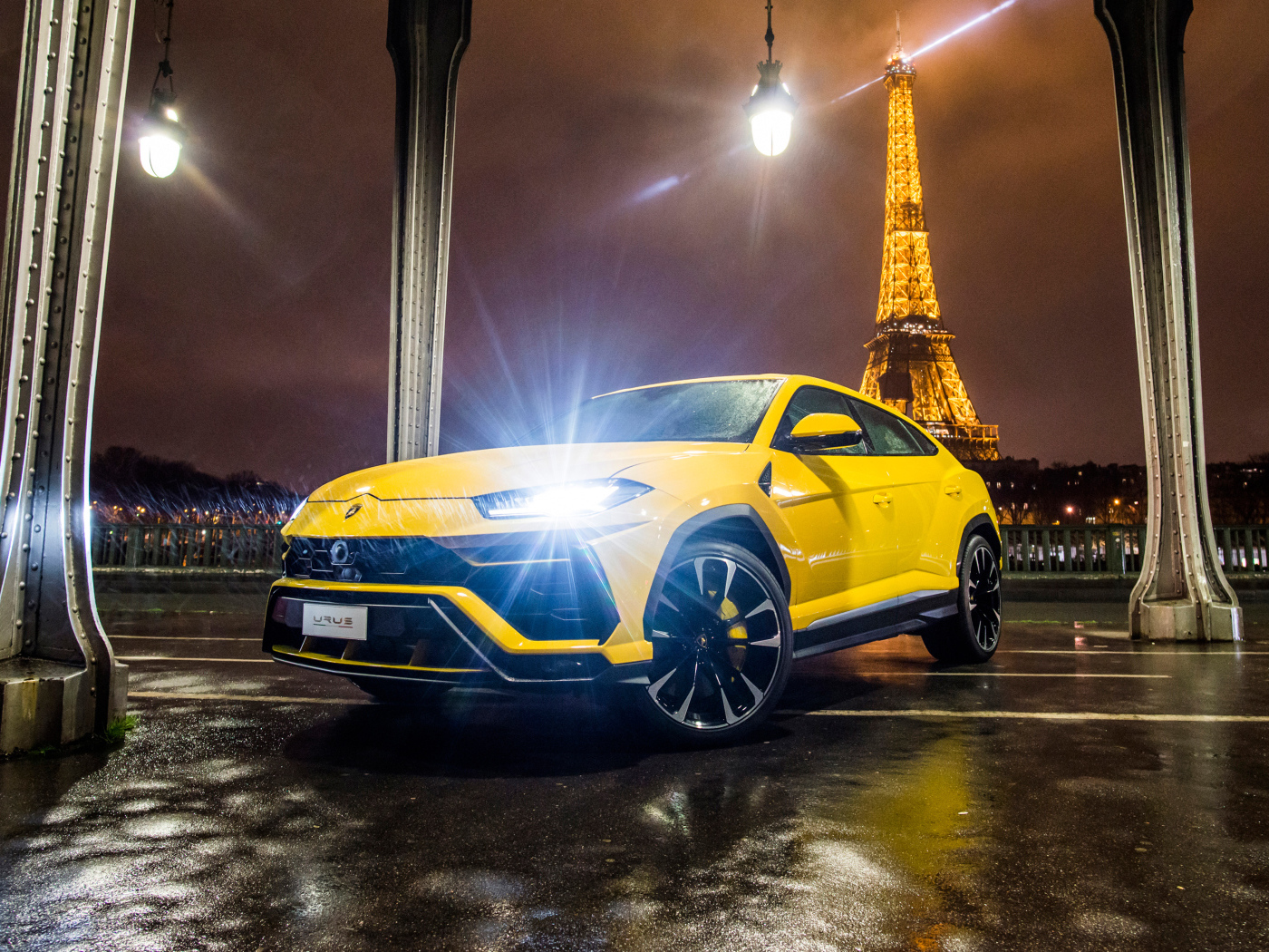 Желтый Lamborghini Urus, 2018 с включенными фарами на фоне Эйфелевой башни