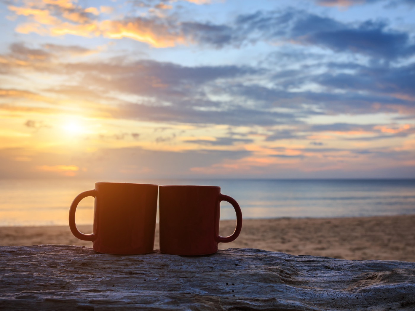 Две чашки стоят на песке на фоне рассвета 