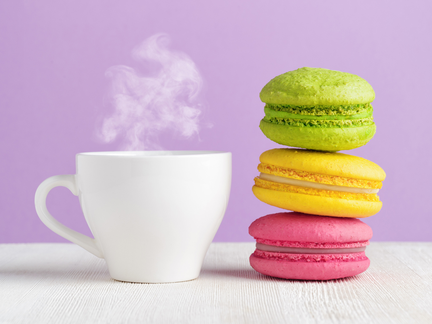 Разноцветный десерт макарун с чашкой горячего кофе на столе