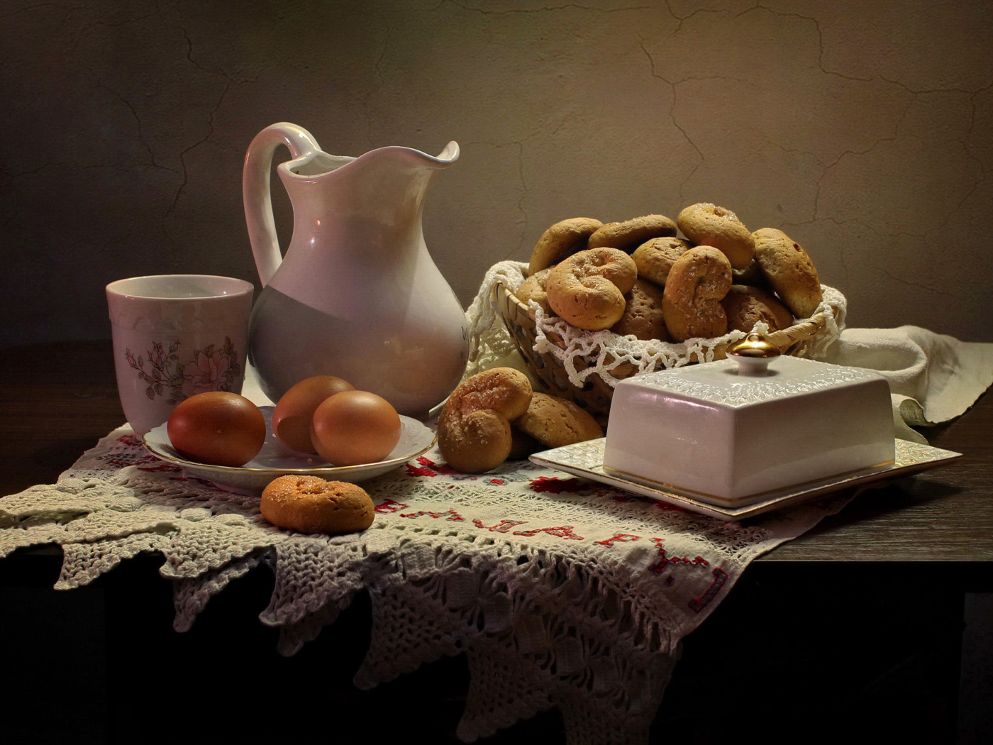 Вареные яйца на столе с кувшином, выпечкой и масленкой 