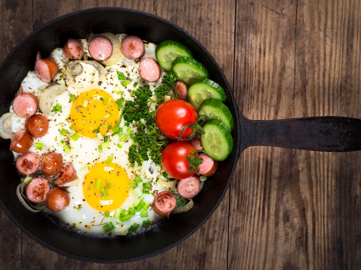 Яичница в сковороде с овощами и кусочками сосиски
