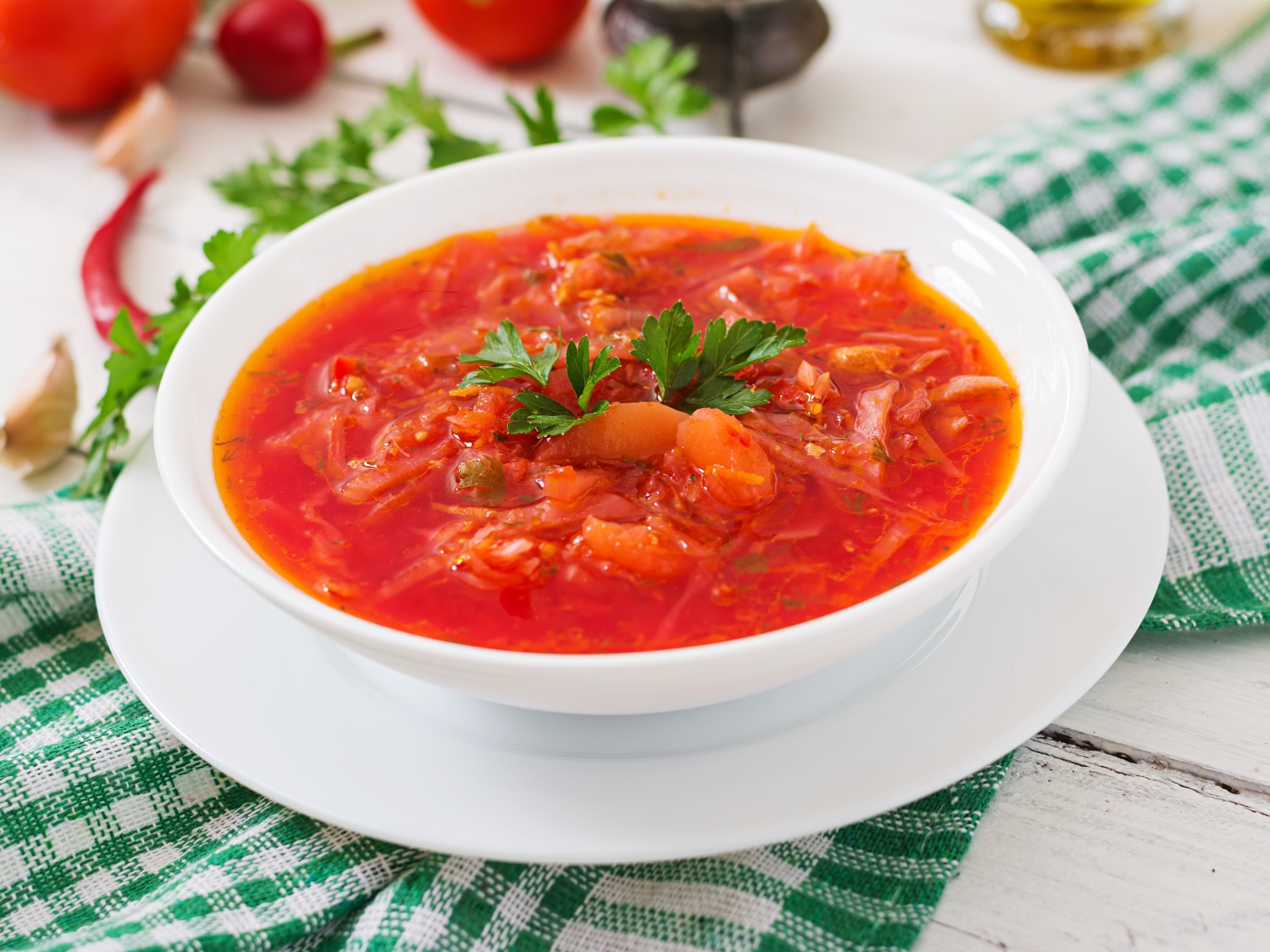 Горячий борщ с зеленью в белой тарелке на столе