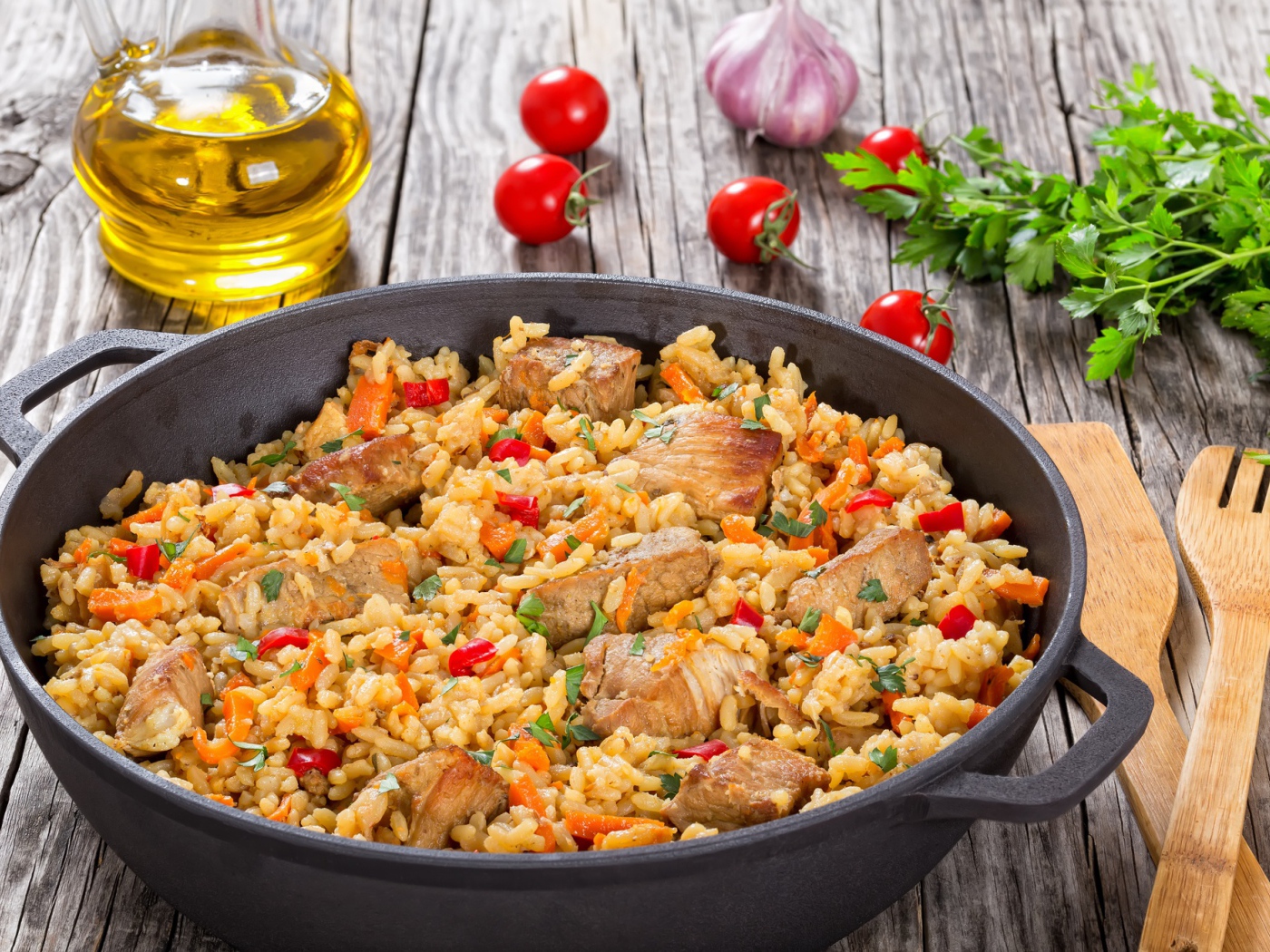 Плов с мясом на столе с помидорами и зеленью петрушки