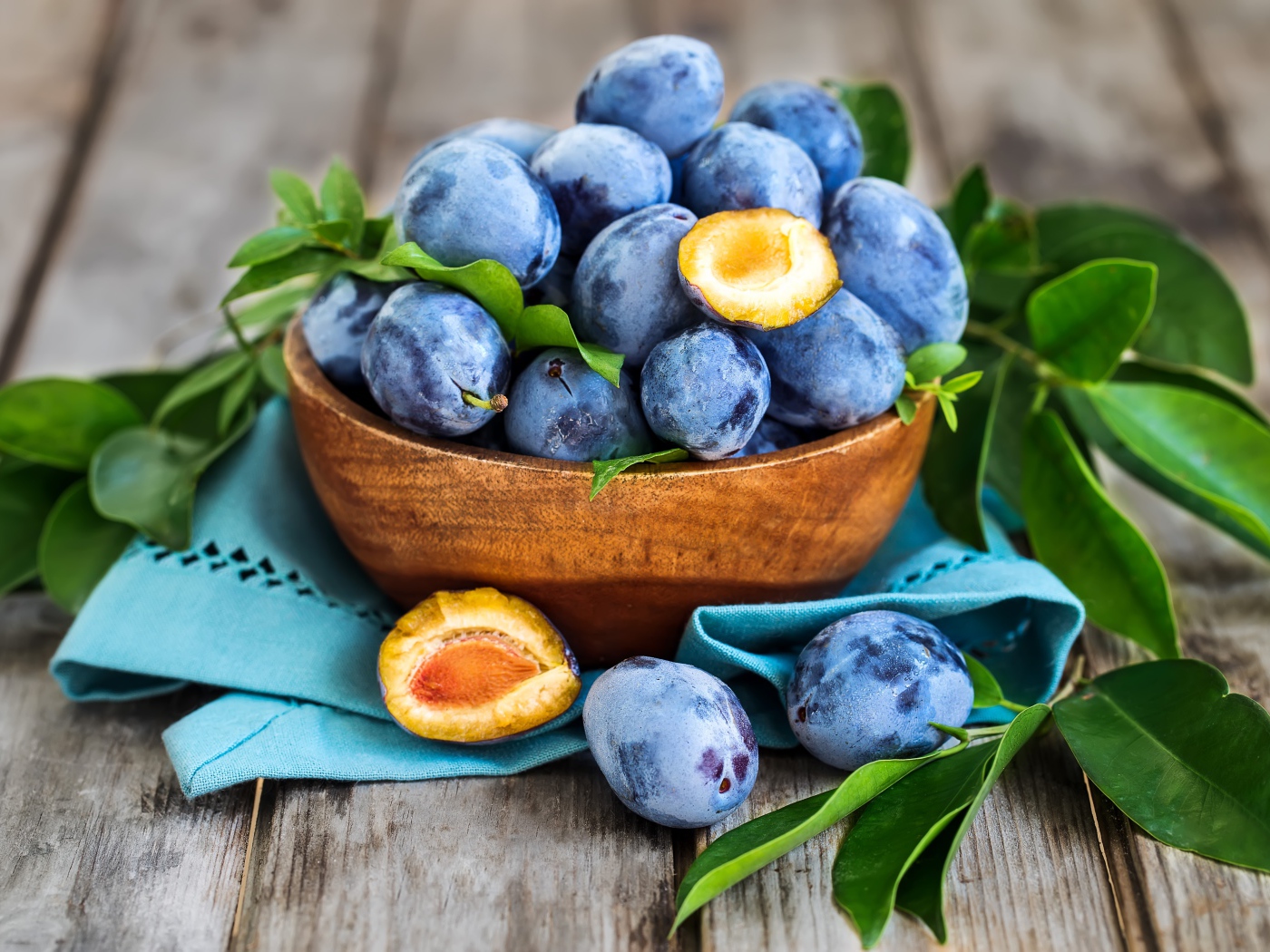 Синие сливы в деревянной миске с зеленой листвой