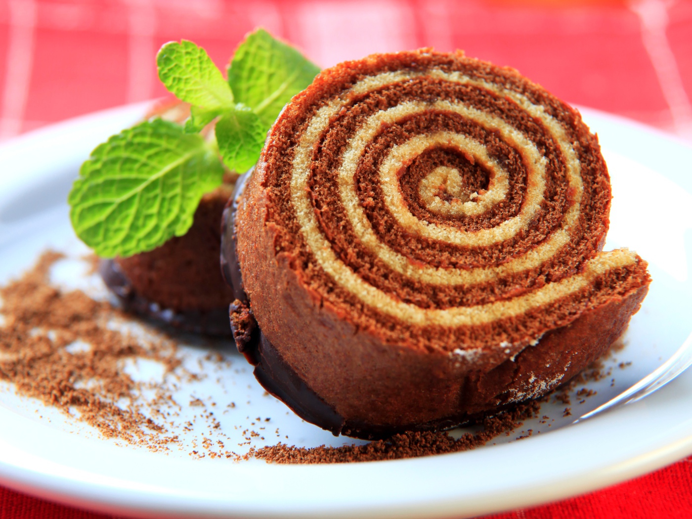 Кусок сладкого рулета с шоколадом и листом мяты на тарелке