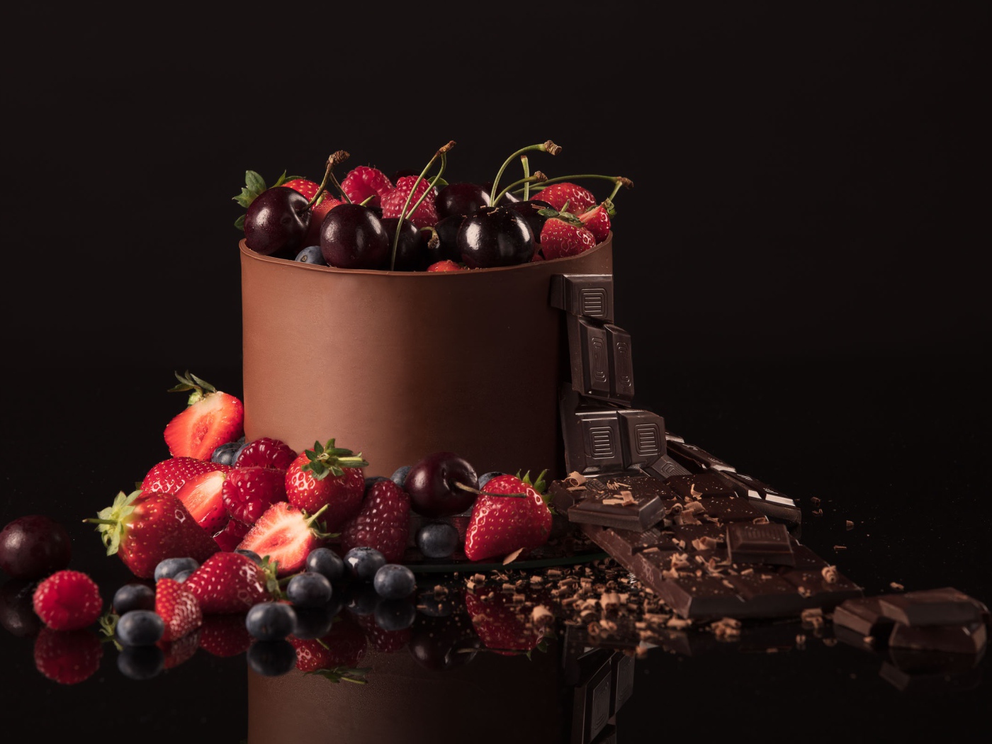 Черный шоколад с ягодами черники, малины, клубники и вишни на черном фоне