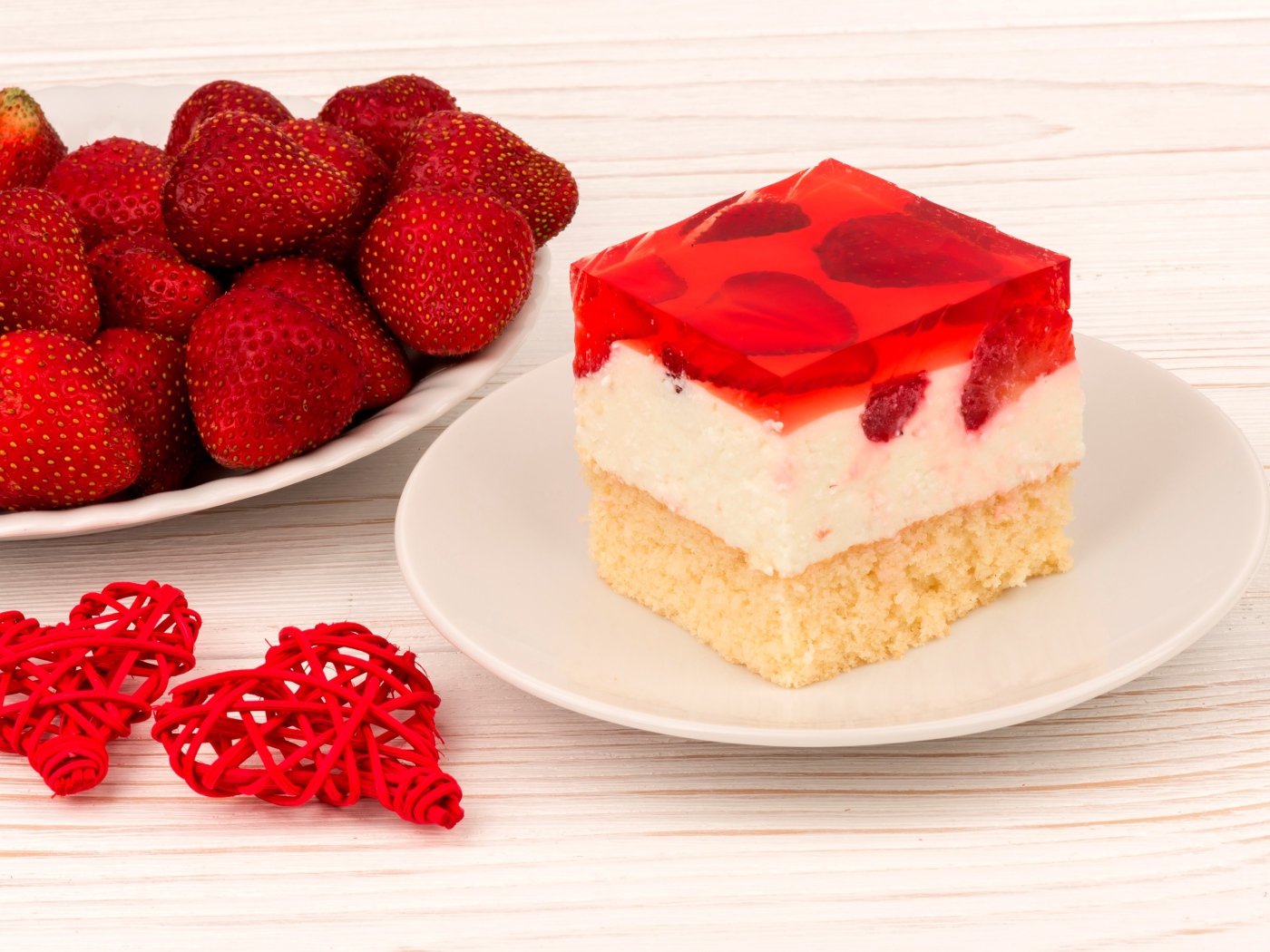 Пирожное на столе с клубникой и красными плетеными сердечками