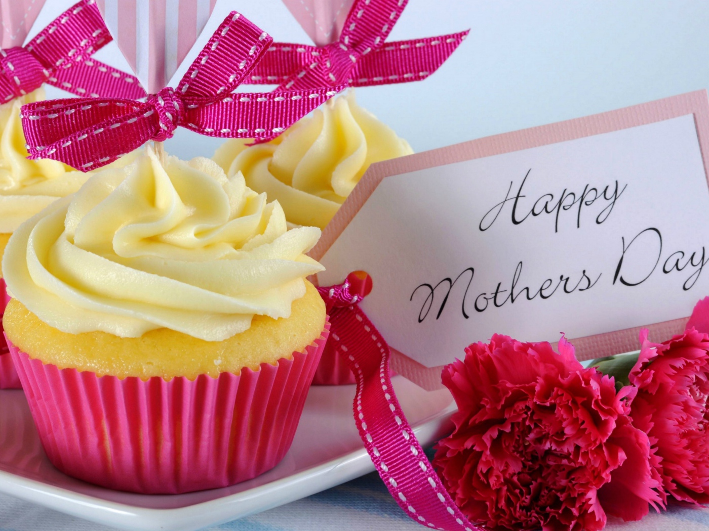Кексы с кремом рядом с гвоздиками и пожеланиями к Дню матери
