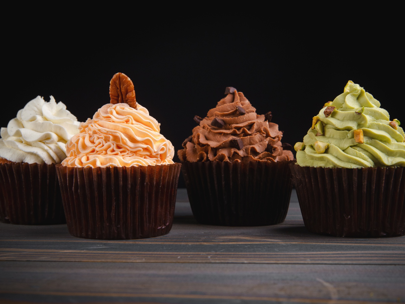 Четыре аппетитных капкейка с кремом на черном фоне