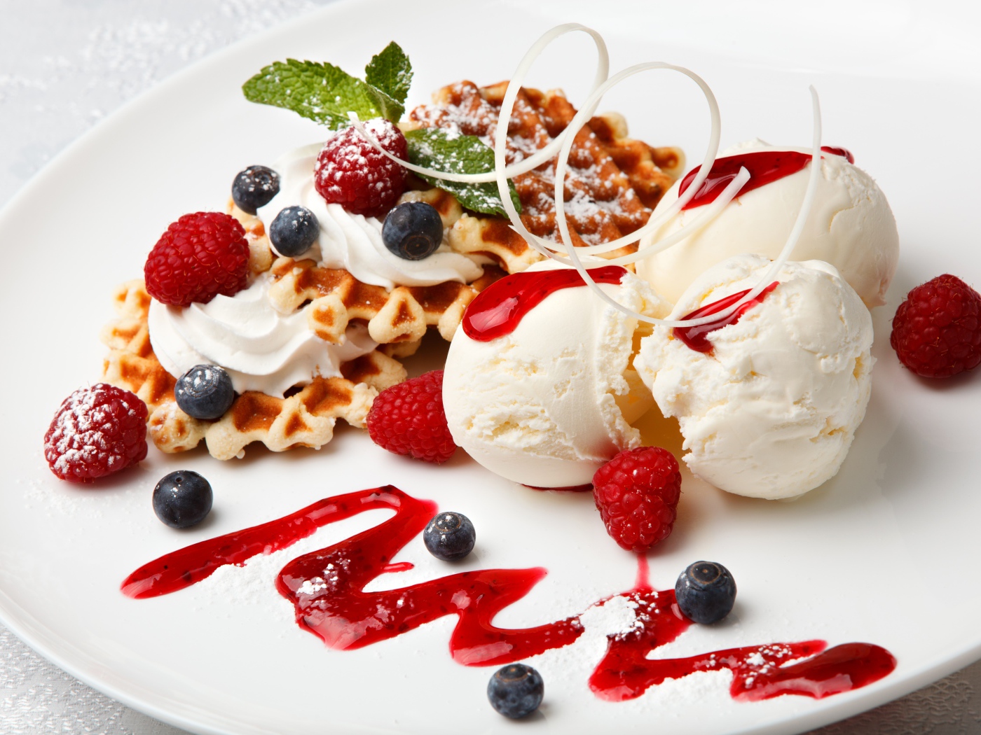 Сладкие вафли с ягодами черники и малины на белой тарелки с шариками мороженого