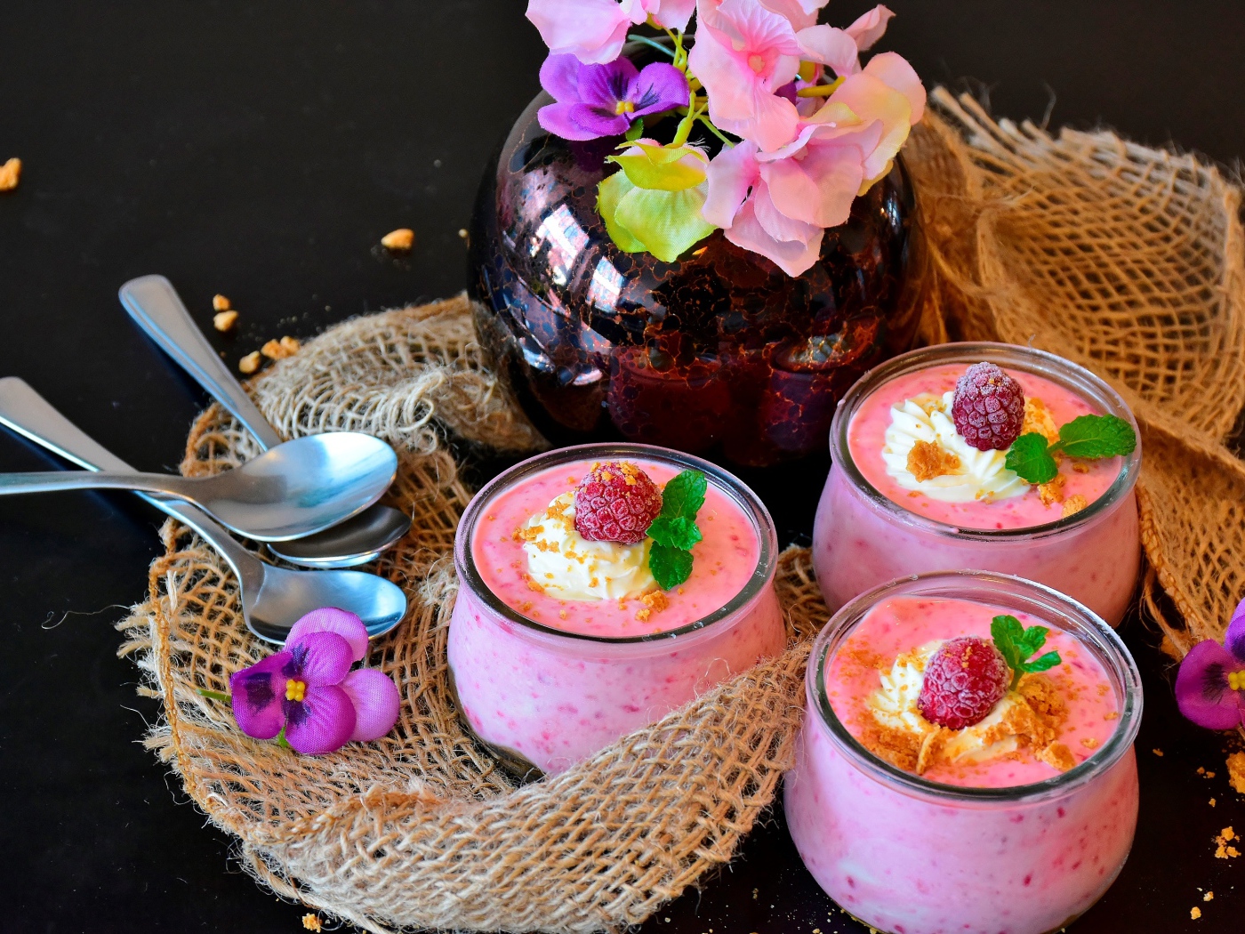 Три банки десерта с малиной на столе с цветами