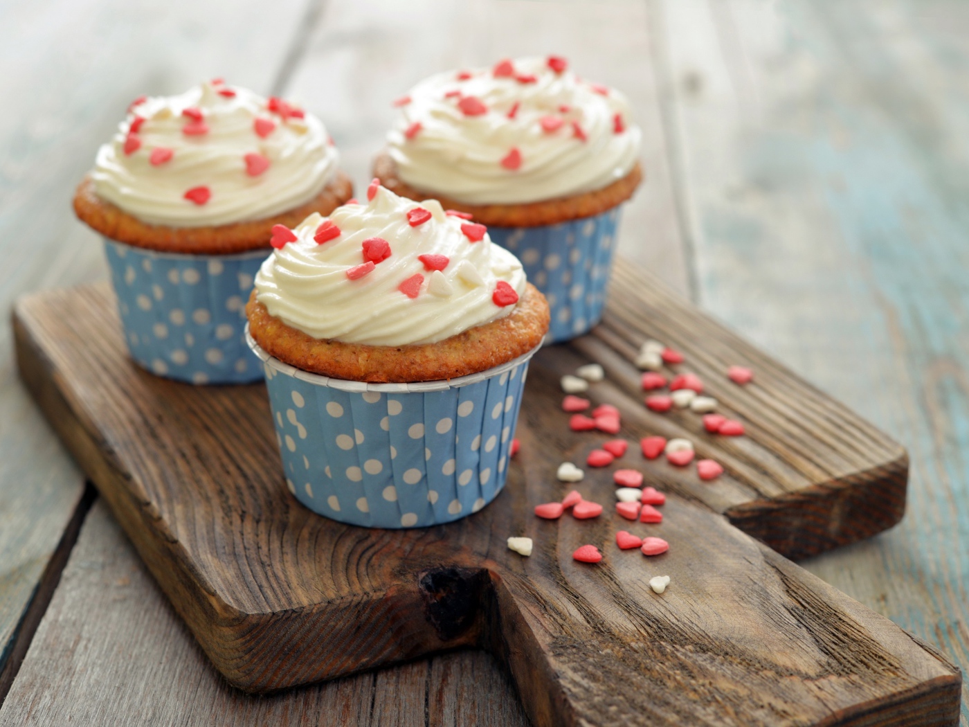 Три кекса со сливками украшены сердечками стоят на разделочной доске