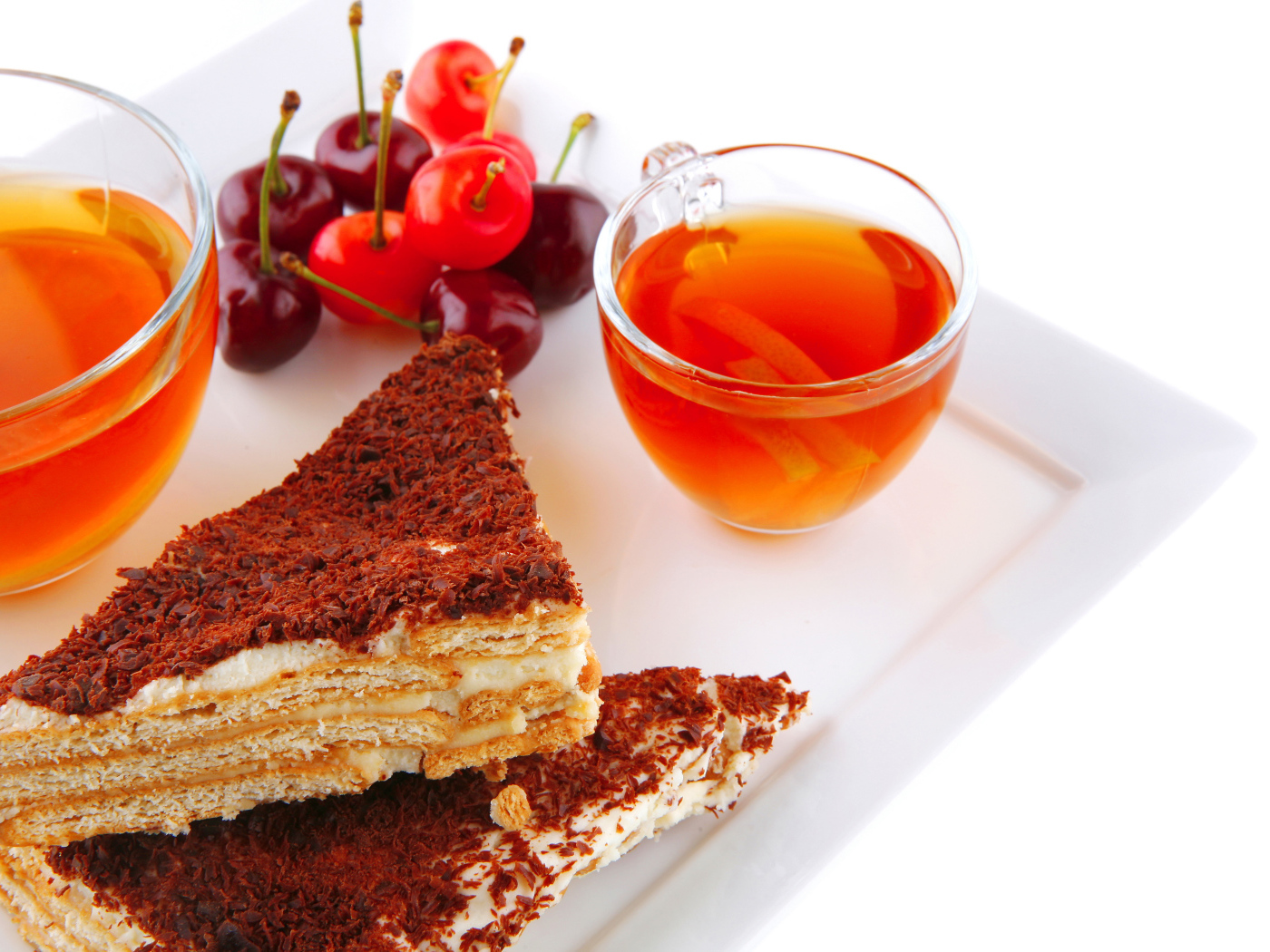 Два кусочка пирожного на столе с чаем и вишнями на белом фоне