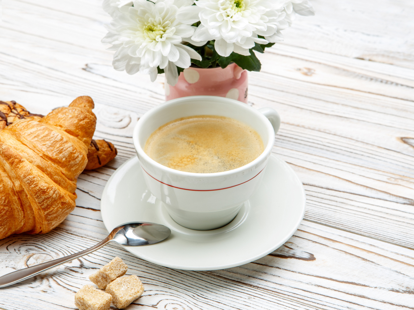 Чашка кофе и круассаны на столе с белыми хризантемами 