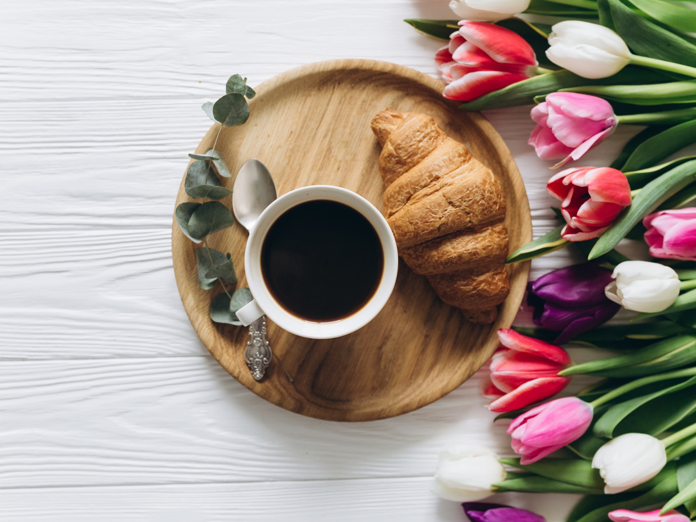 Чашка кофе с круассаном на столе с букетом тюльпанов 