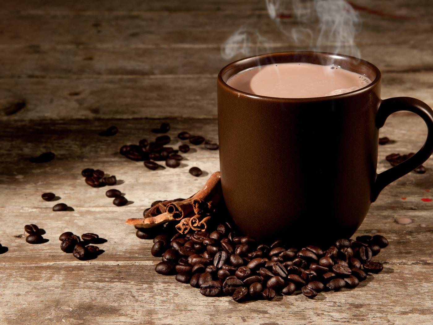 Чашка горячего кофе с молоком на столе с корицей и кофейными зернами