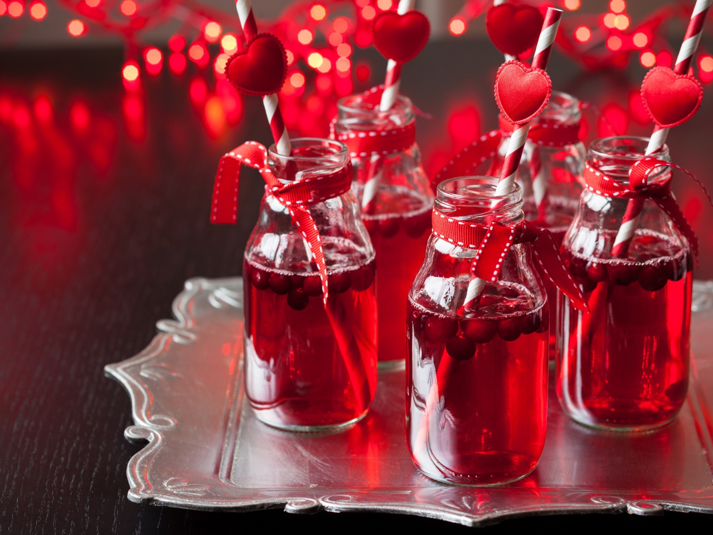 Вкусный напиток с клюквой в стеклянных бутылках на столе с трубочками