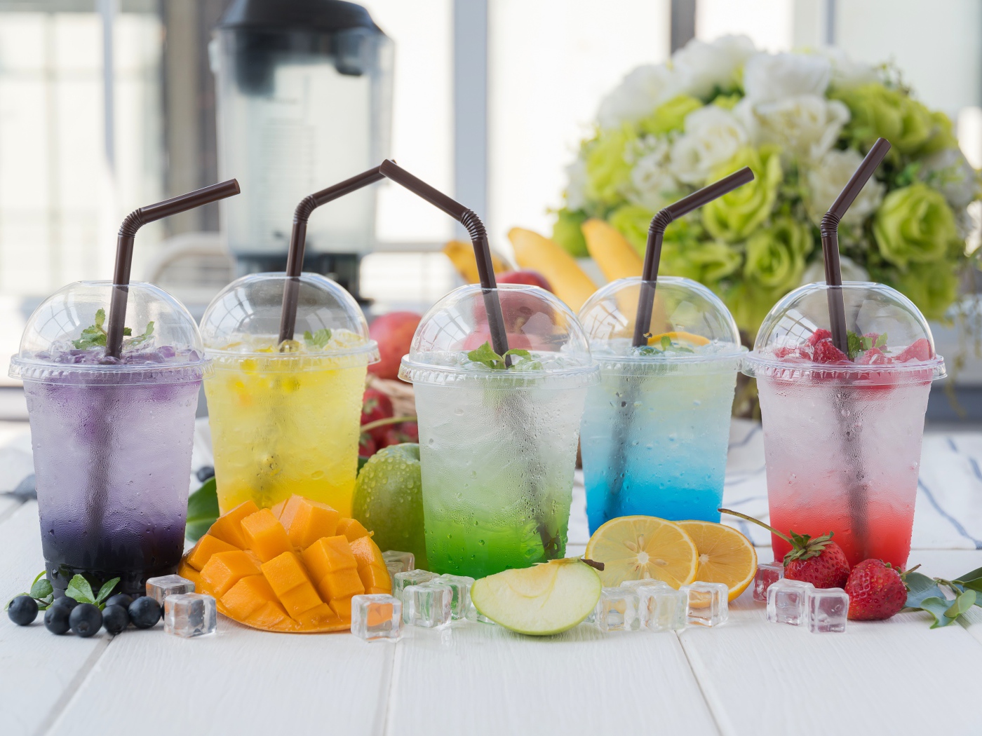 Коктейли в стаканах с трубочками на столе с кубиками льда и фруктами