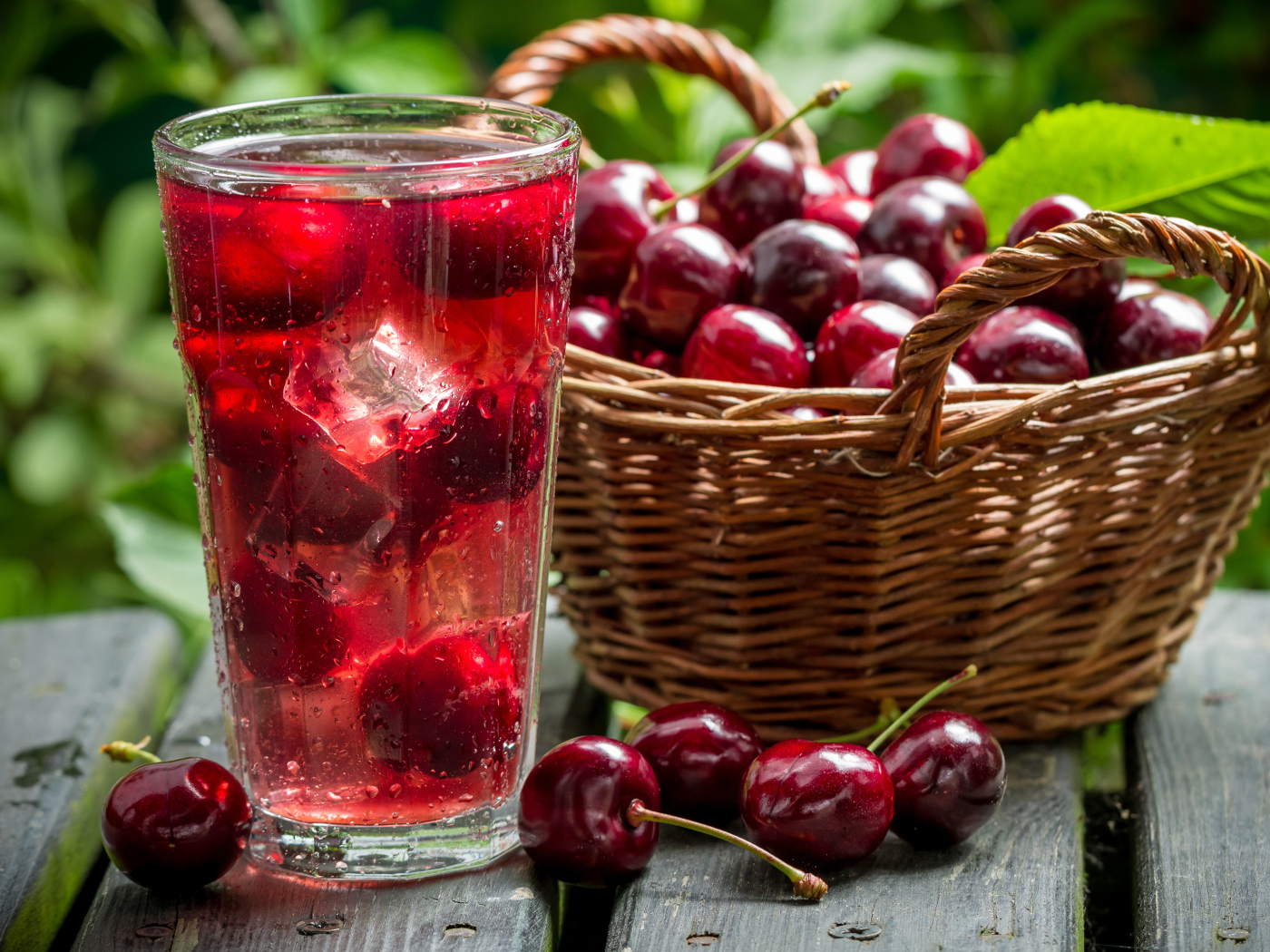 Стакан напитка со льдом на столе с корзиной с черешней 