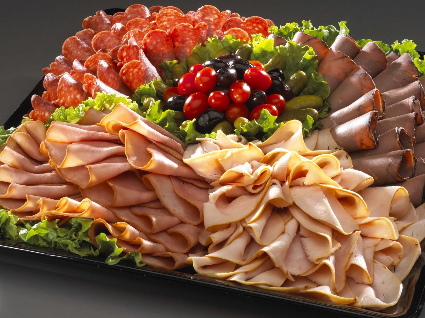 Большое блюдо с аппетитной мясной нарезкой, листьями салата и оливками