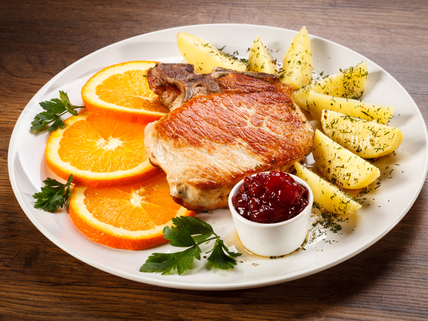 Кусок запеченного мяса с кусочками картофеля и апельсина и соусом