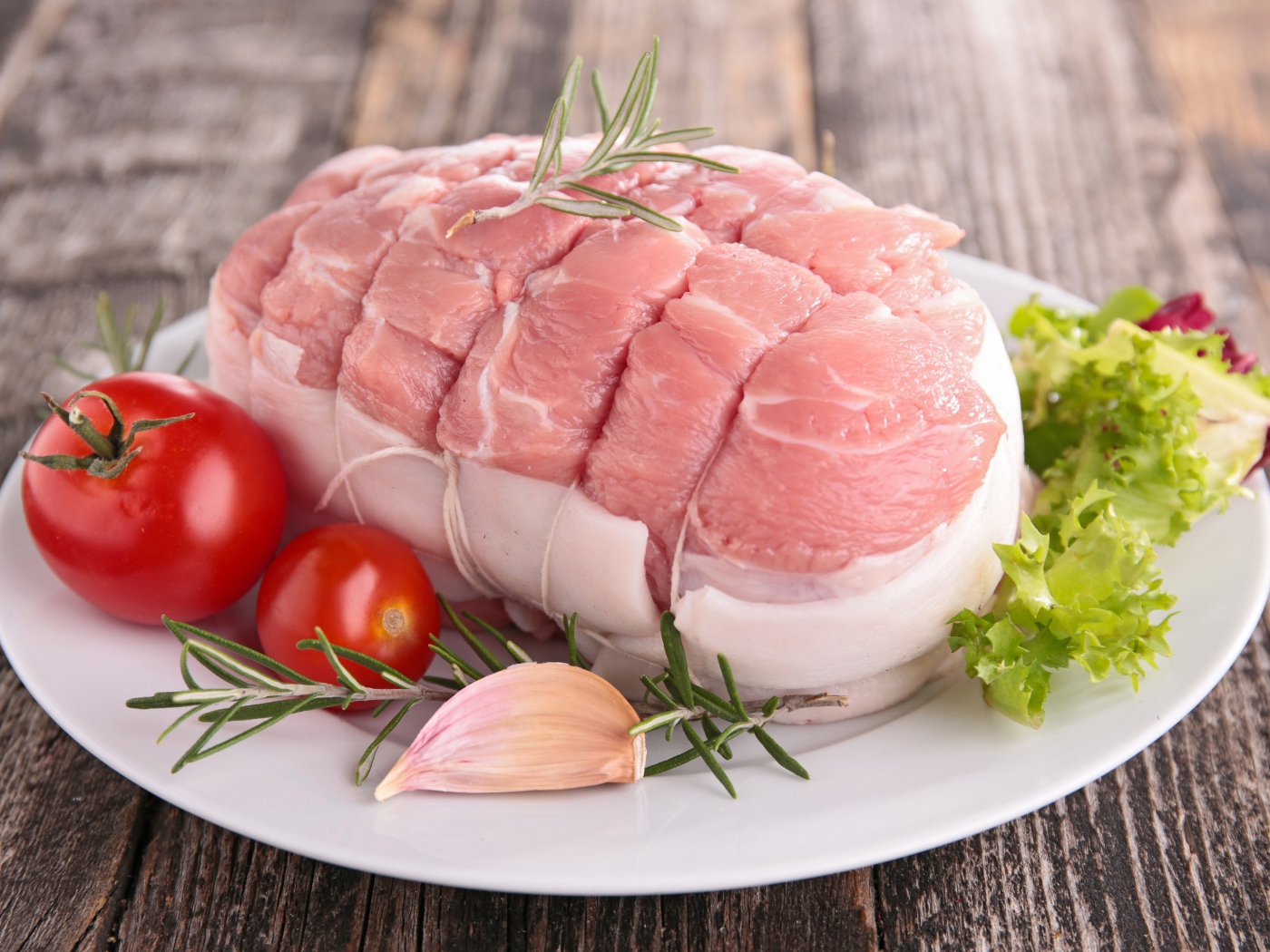 Кусок свежего мяса со свежими помидорами, чесноком и листьями салата