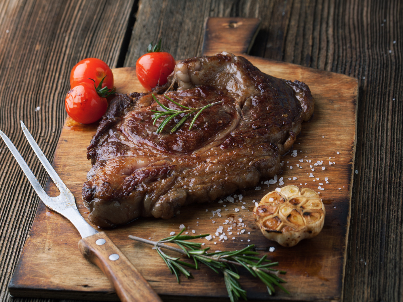 Кусок жареного мяса на разделочной доске с помидорами и чесноком