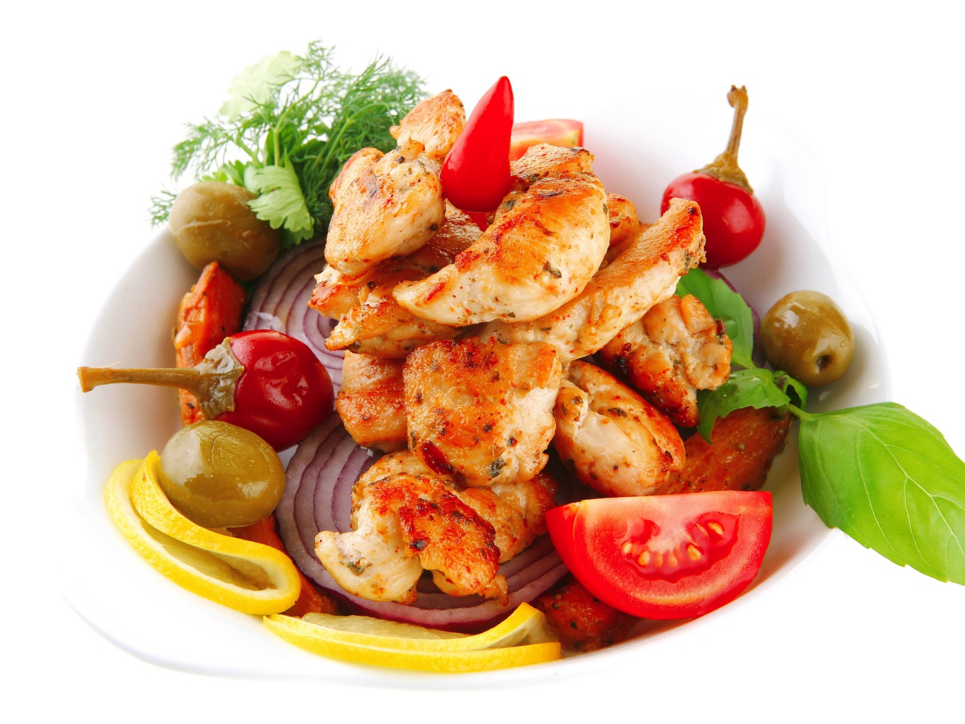 Жареные кусочки курицы на тарелке с овощами и зеленью 