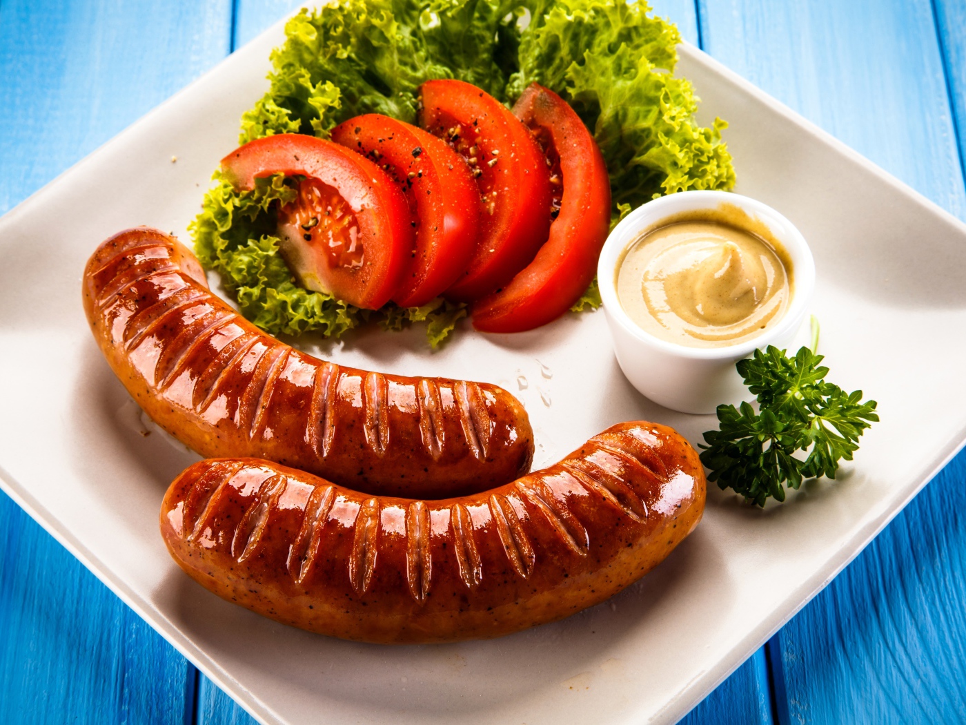 Две сосиски гриль на тарелке с овощами и горчицей