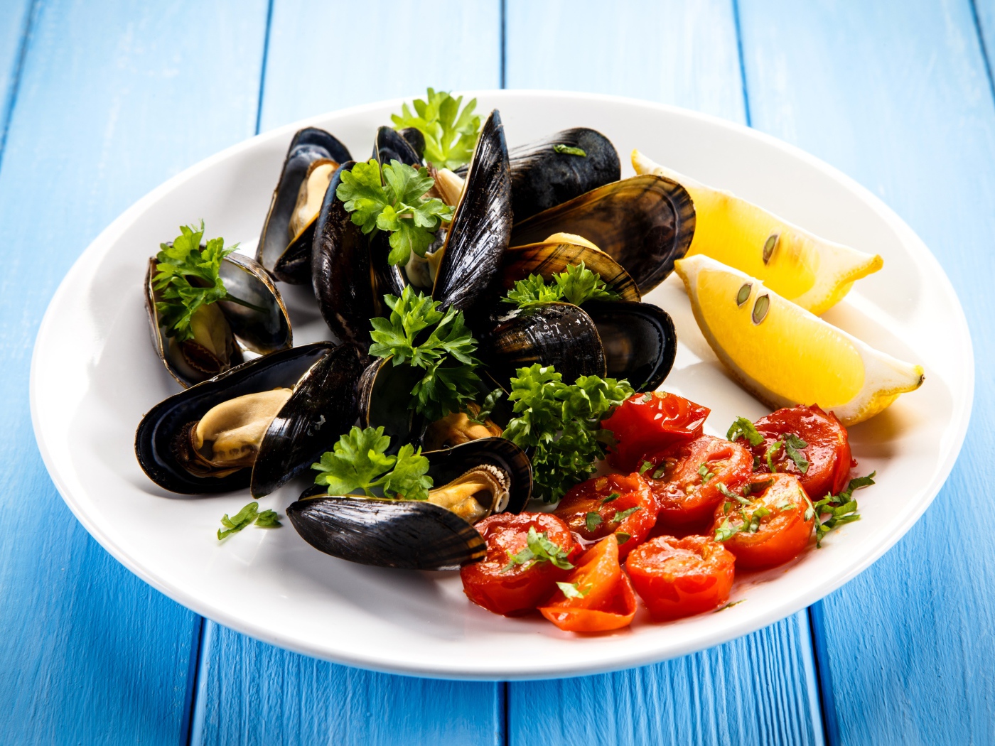 Мидии с томатами, кусочками лимона и зеленью петрушки на белой тарелке