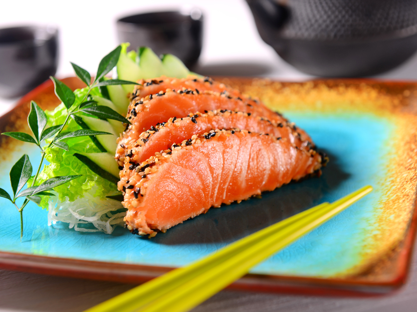 Красная рыба с листьями салата и свежими огурцами на тарелке с палочками