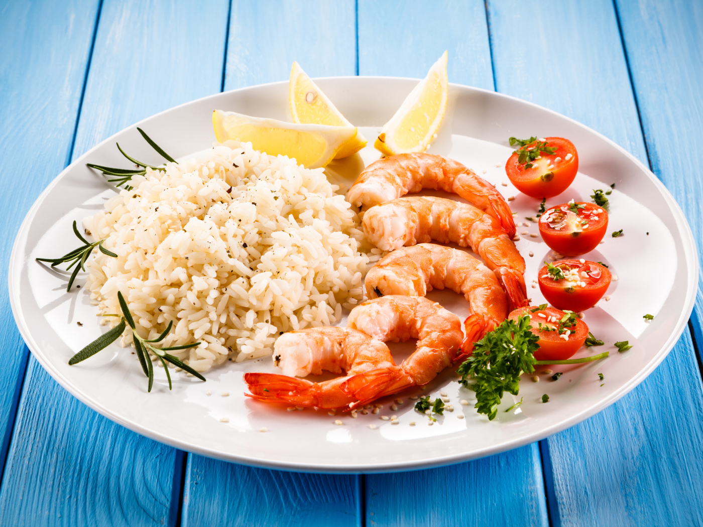 Креветки на тарелке с рисом, помидорами и лимоном