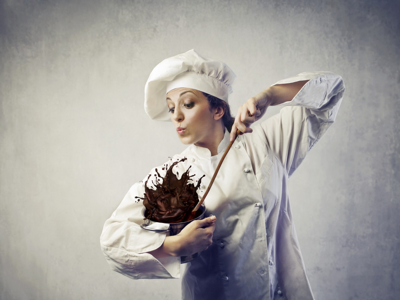 Женщина повар мешает шоколад в посуде на сером фоне