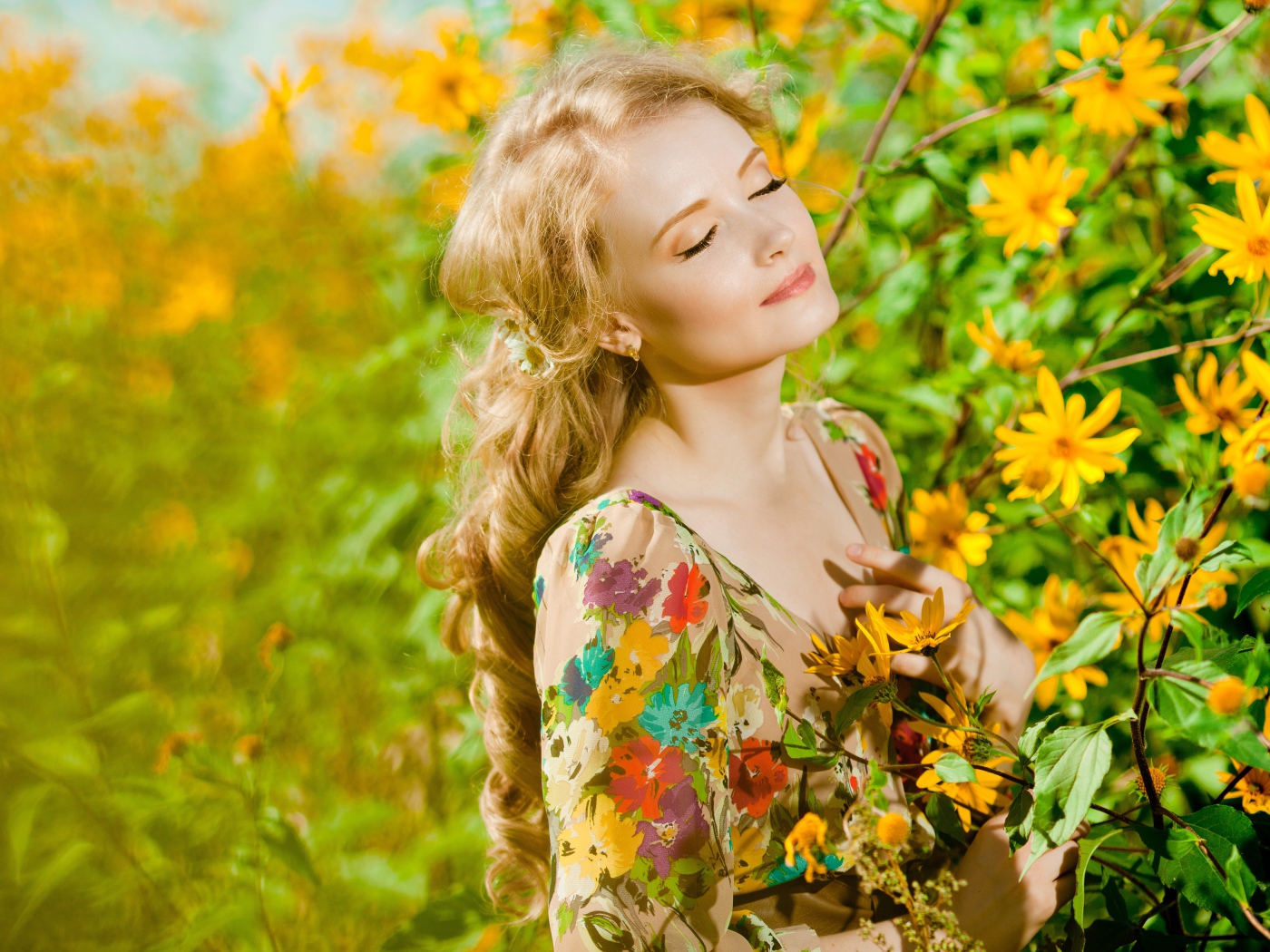 Красивая блондинка нежится в лучах солнца у желтых цветов