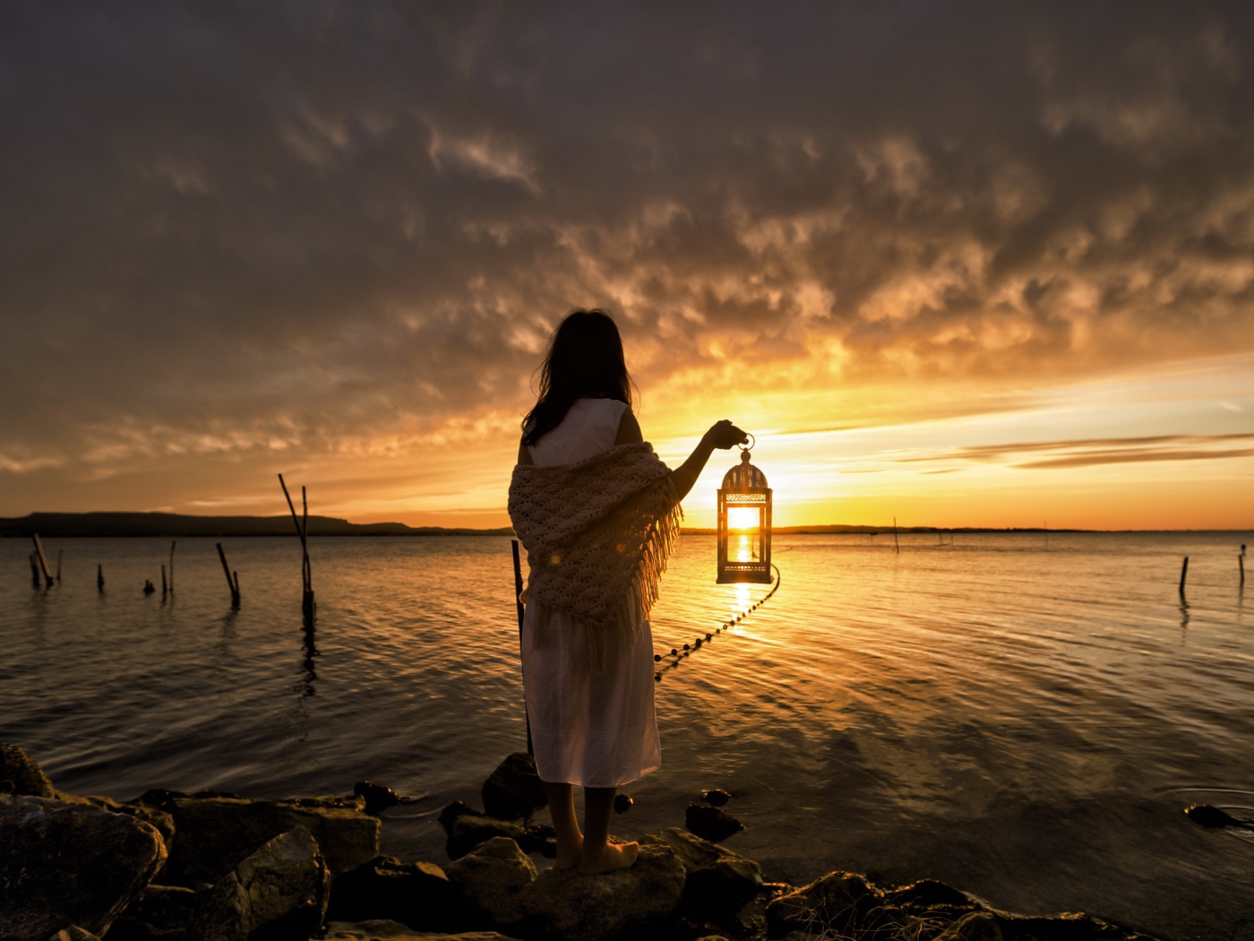 Девушка в белом платье стоит у воды с фонарем