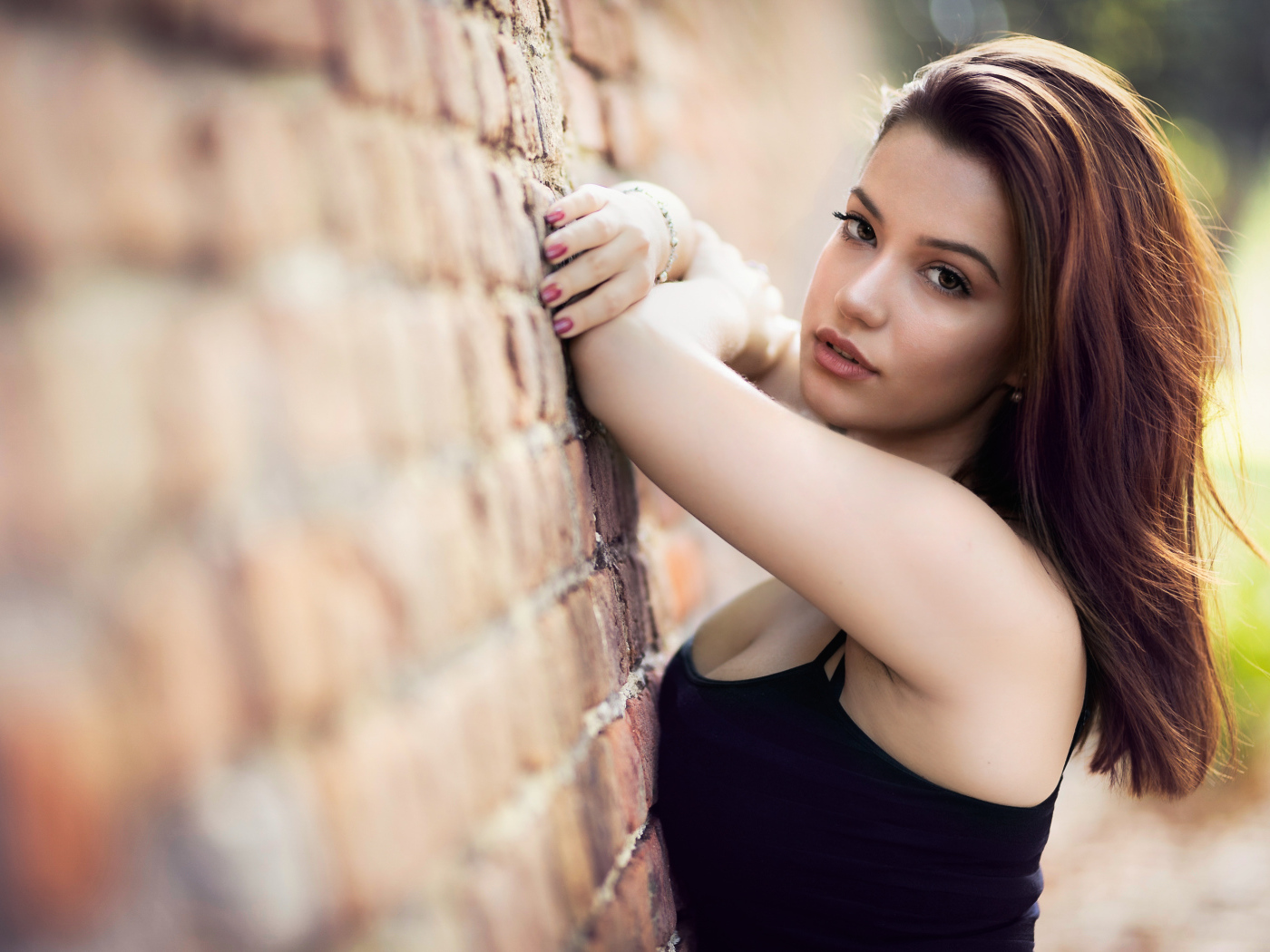 Нежная  девушка шатенка стоит у кирпичной стены