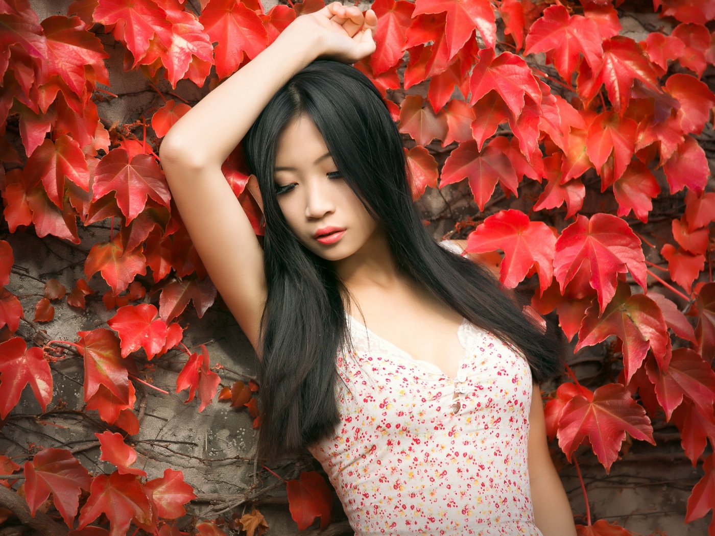 Молодая девушка азиатка стоит у стены с красными листьями