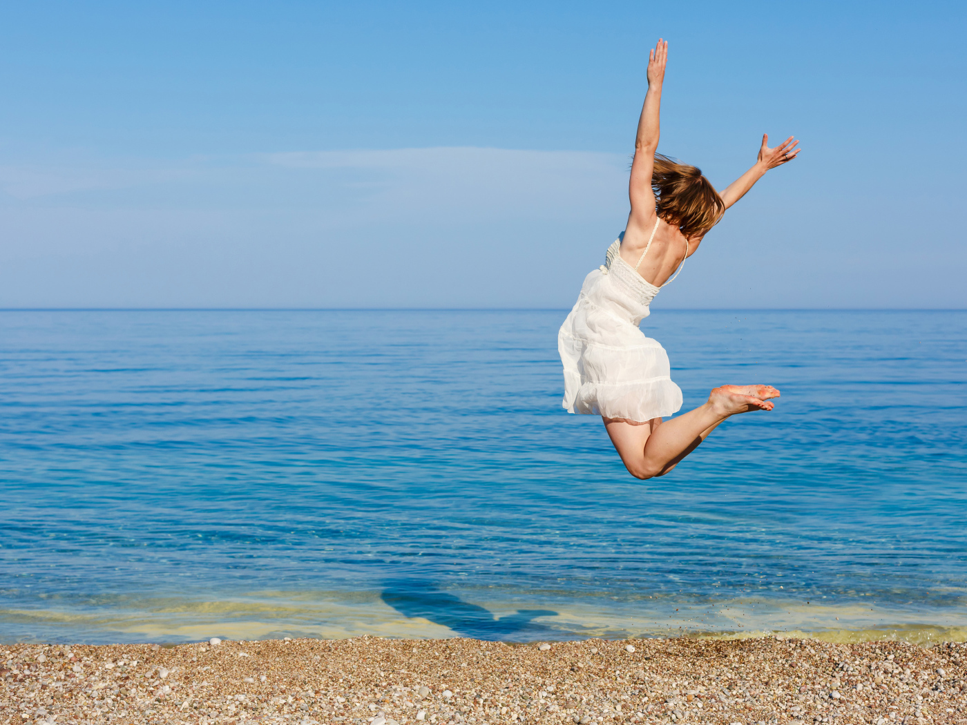 Молодая девушка в белом платье делаем прыжок на песке у моря